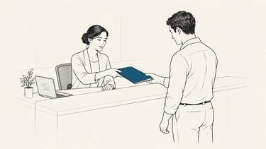 An employee hands a customer a folder while the laptop stays to one side.